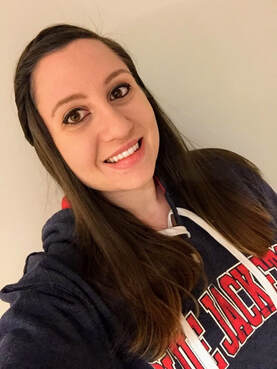 Woman with dark brunette hair smiling in a selfie. She wears a sweatshirt for the hockey team, the Columbus Blue Jackets.